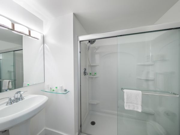 A modern bathroom with a sliding glass shower, vanity sink, mirror, and neatly arranged toiletries.