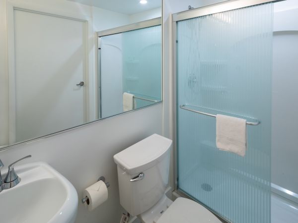 A bathroom with a sink, toilet, and shower with a glass door, featuring a towel hanging on the door.