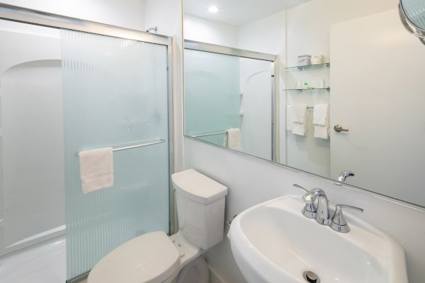 A clean bathroom with a shower, toilet, and sink; large mirror and white towels are visible on the rack and door.