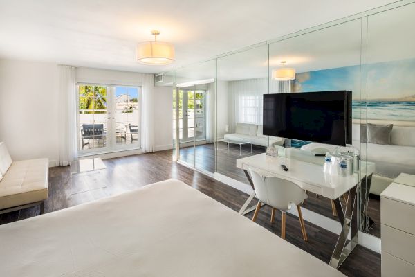 A modern hotel room with a bed, TV, desk, and mirrored wall, featuring a bright, airy design and an ocean-themed mural.