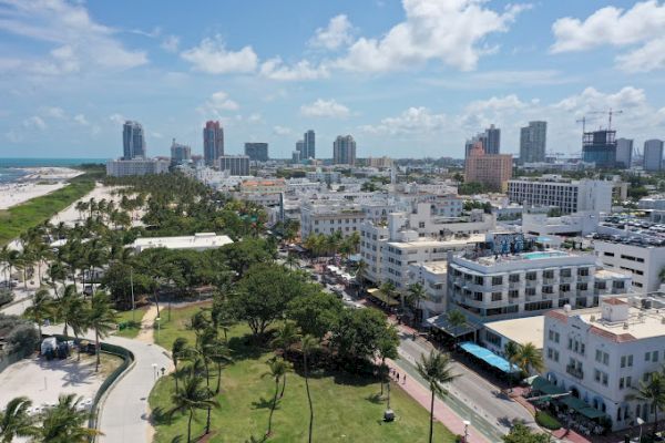 Aerial view of a coastal city with skyscrapers, green parks, and beaches under a blue sky with clouds.