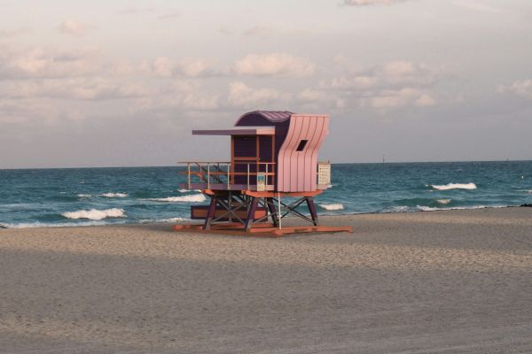 A colorful lifeguard tower on a sandy beach by the ocean under a partly cloudy sky at sunset.