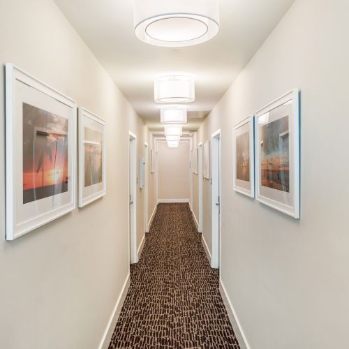 A hallway with framed pictures on both walls, a patterned carpet, and ceiling lights, creating a clean and modern look.